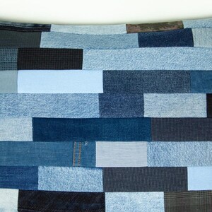May include: A patchwork pillow featuring a variety of denim fabrics in shades of blue, from light to dark. The rectangular pieces are arranged in a brick-like pattern, creating a textured and visually interesting design. The pillow is a unique home decor item.