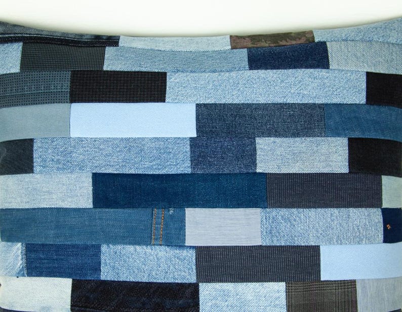 May include: A patchwork pillow featuring a variety of denim fabrics in shades of blue, from light to dark. The rectangular pieces are arranged in a brick-like pattern, creating a textured and visually interesting design. The pillow is a unique home decor item.