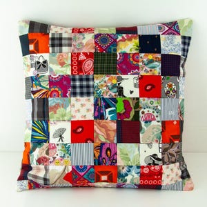 Op de afbeelding: Vierkant patchwork kussen met een verscheidenheid aan stoffen vierkanten in verschillende kleuren en patronen. Het kussen heeft vierkanten van bloemen-, ruit- en gestreepte stoffen, waardoor een levendig en eclectisch ontwerp ontstaat. Een decoratief woonaccessoire.