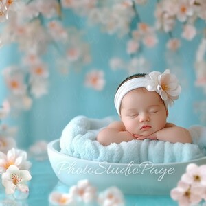 May include: A sleeping baby wearing a white headband with a flower on top, lying in a light blue bowl with a light blue fuzzy blanket. The background is a light blue with white flowers.