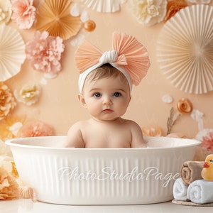 May include: A baby wearing a pink bow headband sits in a white bathtub with a yellow rubber ducky and towels on the edge. The background is a peach wall with paper flowers.