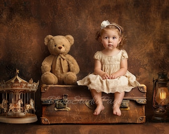May include: A young girl in a white dress sits on a vintage suitcase with a teddy bear beside her. A carousel and a lantern are on either side of the suitcase. The background is a brown textured wall.