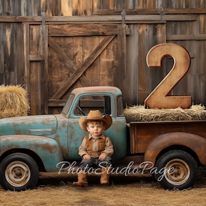 Peut inclure: Un jeune enfant portant un chapeau de cowboy est assis dans la benne d'un camion pick-up bleu et rouillé. Le camion est garé devant une grange en bois avec un grand numéro 2 en bois à l'arrière de la benne.