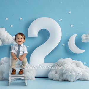 May include: A young boy wearing a white shirt and a blue tie sits on a white chair in front of a large white number two. The background is a light blue with white clouds and stars.