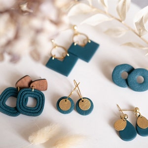 Könnte beinhalten: Fünf Paar Ohrringe aus tealblauem Polymer Clay mit goldenen Akzenten. Die Ohrringe werden auf einer weißen Oberfläche präsentiert.