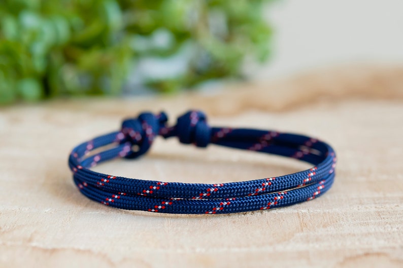 Pu&ograve; includere: Un braccialetto in corda blu navy e rosso con chiusura a nodo. Il braccialetto &egrave; realizzato con una corda spessa e resistente e presenta un sottile motivo rosso e bianco.