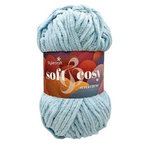 May include: A ball of light blue super chunky yarn with a textured, velvet-like appearance. The centre is wrapped in a paper label featuring the text Stylecraft soft & cosy SUPER CHUNKY over a background of overlapping colourful abstract shapes.