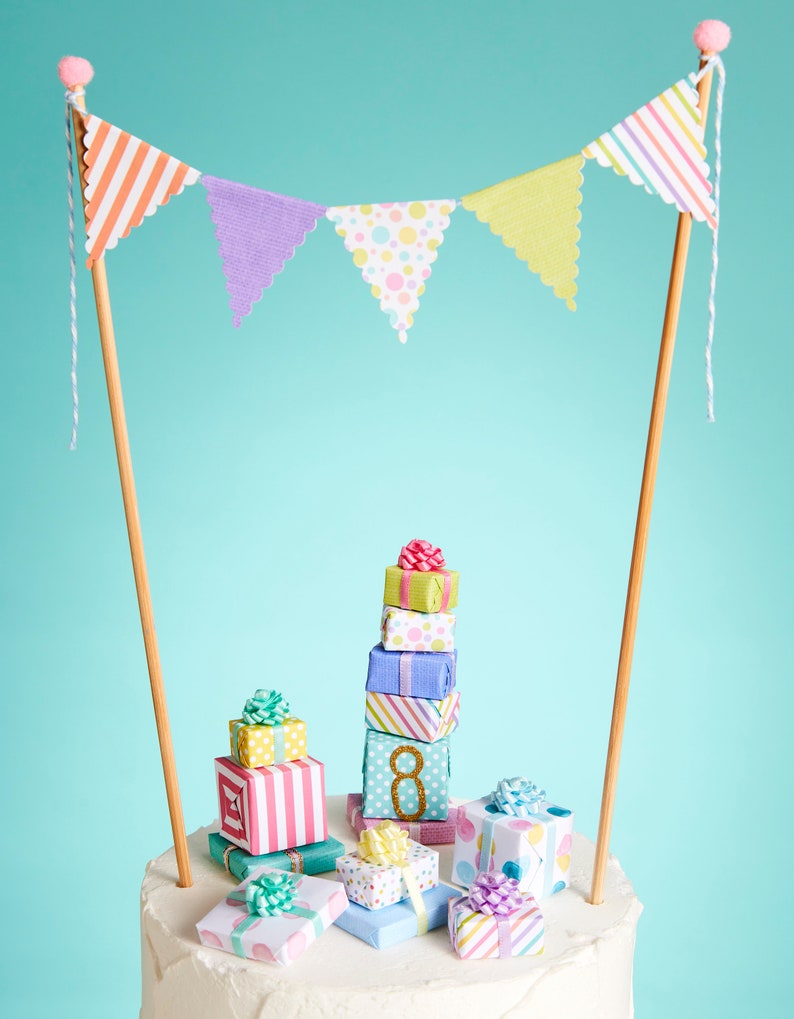 May include: A white cake decorated with a stack of colorful gift boxes and a paper banner with pastel colored triangles. The cake is topped with a number 8.