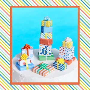 May include: A white cake decorated with colorful, patterned gift boxes. The boxes are stacked in a tower and some are arranged around the cake. The top box has the number "6" on it.