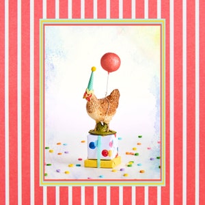 May include: A whimsical figurine of a brown chicken wearing a party hat and holding a red glitter balloon. The chicken stands atop a stack of wrapped gifts with colorful polka dots and ribbons. Confetti is scattered around the base.