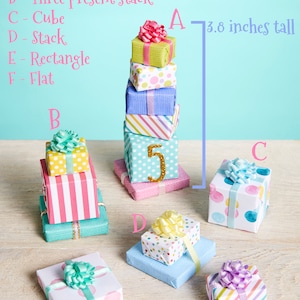 May include: Six miniature gift boxes stacked on top of each other, with a height of 3.8 inches. The boxes are wrapped in various colorful patterns, including polka dots, stripes, and solid colors. The top box has a pink bow. The boxes are labeled A, B, C, D, E, and F.