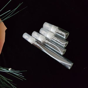 May include: Four clear glass travel-sized spray bottles with silver tops and white sprayers.