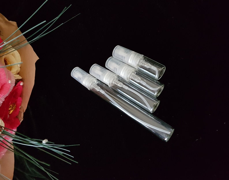 May include: Four clear glass travel-sized spray bottles with silver tops and white sprayers.