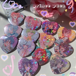 May include: A selection of heart-shaped badges with anime-style character designs. The badges have holographic effects and diverse colour palettes. The text "prince puca" is visible in the background. The badges are displayed on a white surface.