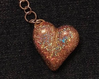 May include: A gold heart-shaped keychain with iridescent glitter. The keychain has a metal chain and a lobster clasp.
