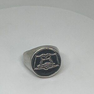 May include: A silver ring with a black oval-shaped stone featuring a stylized owl design.