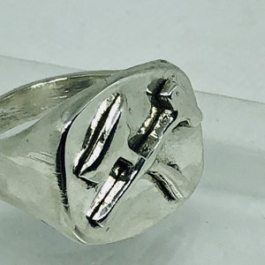 May include: A silver ring with a stylized design of a bird in flight. The ring is made of a smooth, polished metal and has a simple, elegant design.