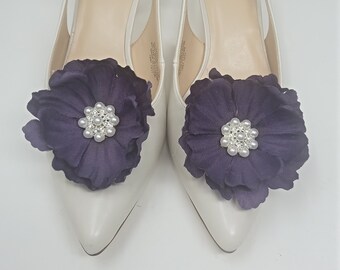 May include: A pair of white leather heeled slingback shoes with a purple flower embellishment on the toe. The shoes are size 7 1/2 and are labeled "Nine West".
