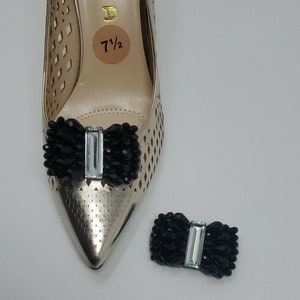 May include: A pair of black shoe clips with a clear rhinestone bow. The clips are shown on a gold shoe with a size 7 1/2 tag.