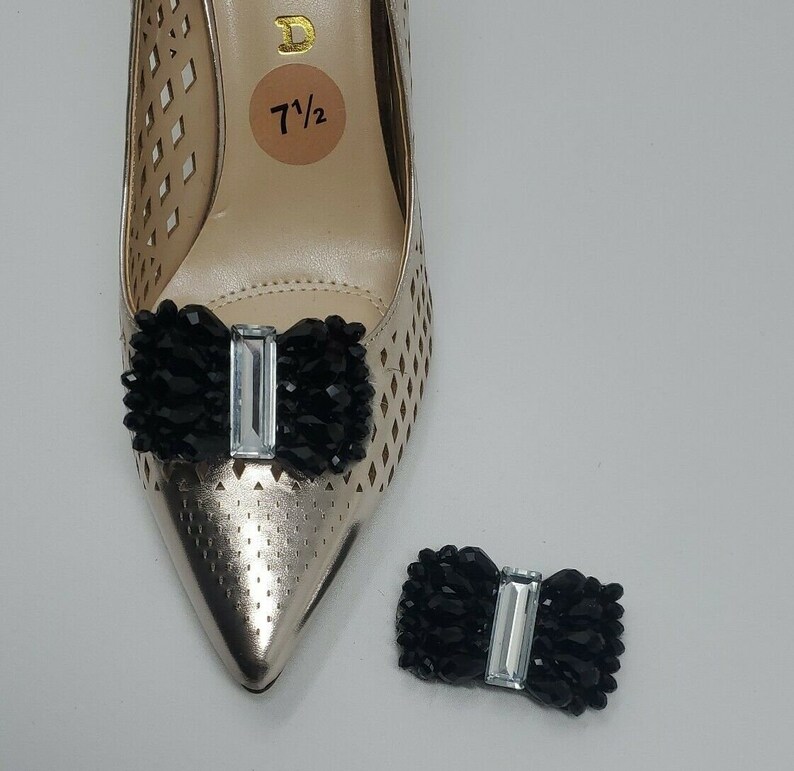 May include: A pair of black shoe clips with a clear rhinestone bow. The clips are shown on a gold shoe with a size 7 1/2 tag.