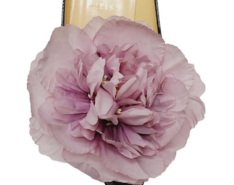 May include: Close-up of a black patent leather shoe with a large, light purple fabric flower attached to the toe. The flower has multiple layers of petals and a darker purple center. The word "Paris" is visible on the insole.