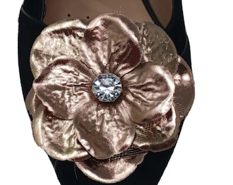 May include: Black pointed-toe shoe with a large, metallic rose-shaped embellishment. The rose is a blend of gold and bronze hues, with a clear, round rhinestone center. The shoe's upper is black.