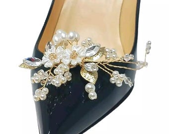May include: Close-up of a black patent leather high-heeled shoe adorned with a floral embellishment. The decorative piece features white flowers, pearls, gold-colored leaves, and sparkling crystals. The word "Paris" is visible on the insole.