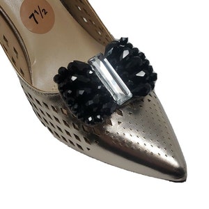 May include: Gold shoe with a black and clear crystal bow embellishment. The shoe has a size tag that says "7 1/2".