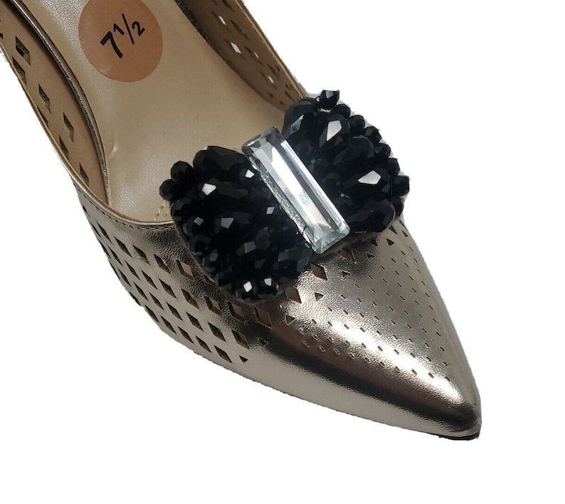 May include: Gold shoe with a black and clear crystal bow embellishment. The shoe has a size tag that says "7 1/2".