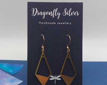 May include: A pair of gold-toned geometric drop earrings with a diamond-shaped cutout design, suspended from gold-toned hooks. The earrings are displayed on a dark blue card featuring the text Dragonfly Silver Handmade Jewellery.