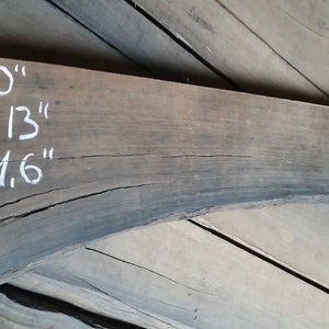 May include: A dark brown wooden plank with white chalk markings indicating the length as 60 inches, width as 13 inches, and thickness as 1.6 inches. The plank is curved and has a rough texture.