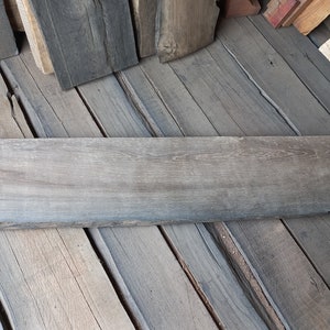 May include: A long, dark gray wooden plank with a light gray number "68-11" written on the top left corner. The plank is lying on a surface of similar wooden planks.