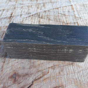 May include: A dark gray wooden block with a natural wood grain pattern. The block is rectangular and has a smooth surface.