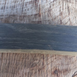 May include: A dark gray rectangular block of wood with a smooth surface and visible grain.