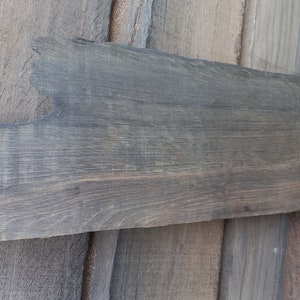 May include: A long, narrow piece of reclaimed wood with a gray stain. The wood has a rough, rustic texture and is perfect for crafting.