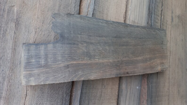 May include: A long, narrow piece of reclaimed wood with a gray stain. The wood has a rough, rustic texture and is perfect for crafting.