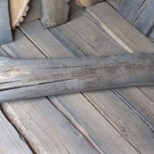 May include: A long, dark gray piece of wood with a natural curve. The wood has a crack running down the center. The wood is labeled "L 64" and "W 13".