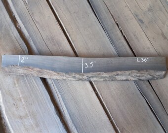 May include: A dark gray wood slab with white markings indicating the dimensions: 2 inches wide, 3.5 inches thick, and 36 inches long.
