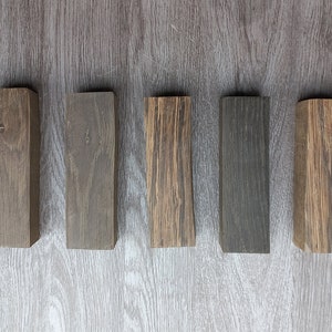 May include: Five wooden blocks in different shades of brown, gray, and black. The blocks are arranged in a row from left to right.