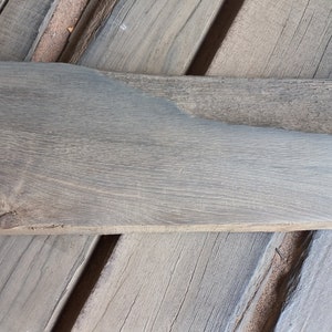 May include: A piece of reclaimed wood, measuring 29 inches long and 9 inches wide, with a gray finish. The wood has a natural grain pattern and a rough texture.