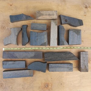 May include: A collection of sixteen assorted dark grey and brown wooden blocks of varying shapes and sizes, arranged in two rows. A yellow measuring tape is positioned horizontally across the centre, showing a length of approximately 66 centimetres.