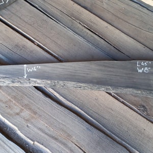 Op de afbeelding: Een donkergrijze houten plaat met een natuurlijke rand. De plaat is 45 inch lang en 8 inch breed. Het hout is ruw en heeft een rustieke uitstraling.