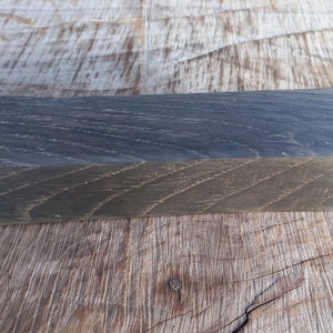 May include: A rectangular block of wood with a dark gray finish, resting on a textured wooden surface. The wood grain is visible, adding to the natural aesthetic. The block's dimensions are approximately 2 x 4 x 8 inches.