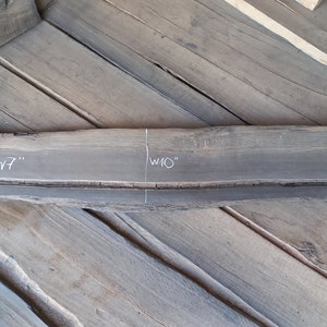 May include: A dark grey wooden plank with visible grain and a rough edge. The plank is labelled with measurements: L55", W7", and W10". The wood appears to be reclaimed or repurposed, with a natural, rustic aesthetic. The plank is approximately 140cm long.
