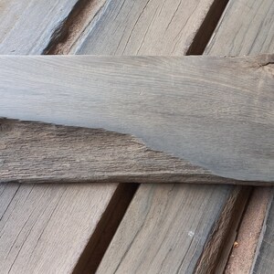 May include: A dark gray wooden plank with a rough, uneven surface. The plank is 17 inches wide and 26.5 inches long.