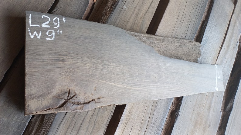 May include: A piece of light gray wood with a knot in the center. The wood is 29 inches long and 9 inches wide.
