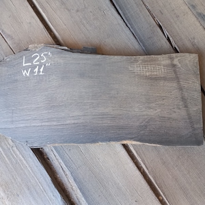 May include: A dark grey wood slab with a rough, natural edge. The slab is marked with white chalk writing: "L 25" and "W 11".
