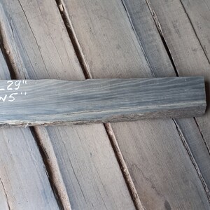 May include: A dark grey wood plank with the text "L29" and "W5" written on it in white. The plank is approximately 74 cm long and 13 cm wide.