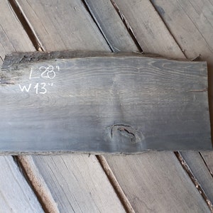 Op de afbeelding: Een donkergrijze houten plaat met een natuurlijke rand, 71 cm lang en 33 cm breed. Het hout heeft een knoop en een natuurlijk houtnerfpatroon.