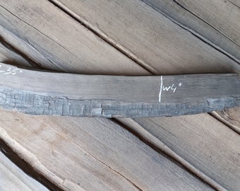 Könnte beinhalten: Ein dunkelgraues Holzstück mit leicht gekrümmter Form. Das Holz hat eine verkohlte, strukturierte Oberfläche. Das Stück ist mit "L35" und "W4" in Weiß markiert.